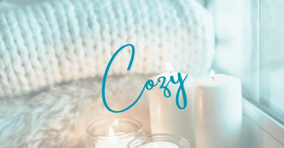 Two thick knitted blankets folded beside a window with candles giving a cozy vibe. The word cozy overlaying the photo.