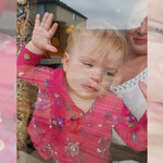 The photo is taken outside with a clear view of Jillian, in a pink floral shirt , pressed up against the glass of the window with her mom smiling in the background.