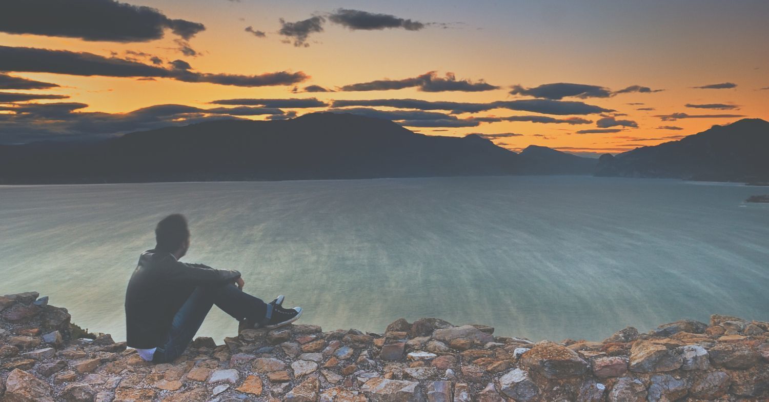 A man reflecting by the water at sunset, symbolizing the journey of understanding thanatology, and coping with grief and loss